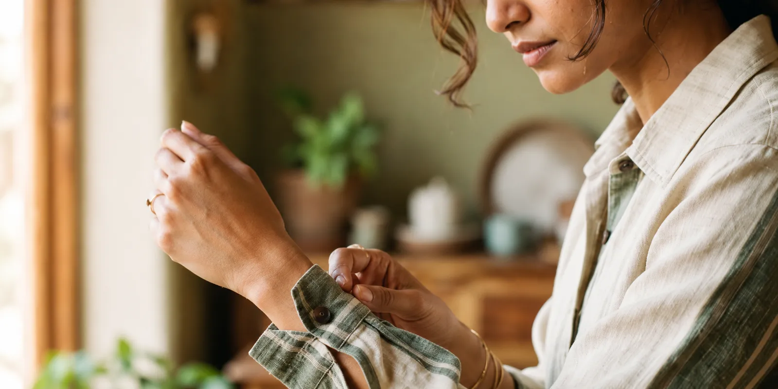 Meera fastening the cuff of a relaxed linen shirt at home